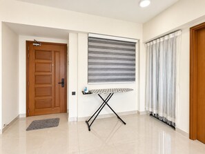 A hallway with a wooden door, a wall-mounted ironing board, and a window with blinds.