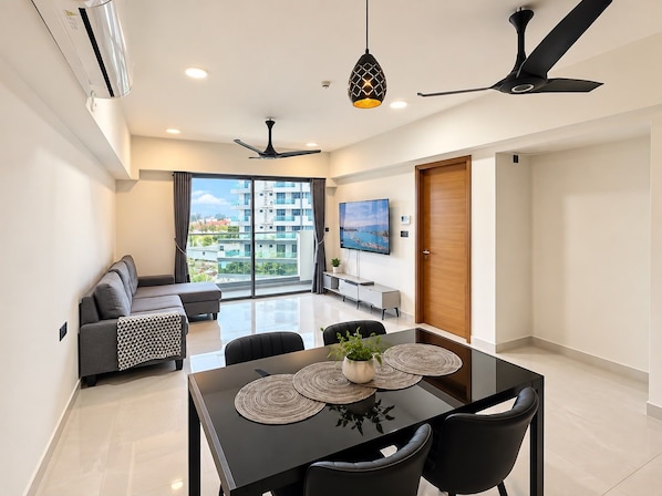 A modern living room with a sofa, dining table with chairs, a TV, and a ceiling fan.