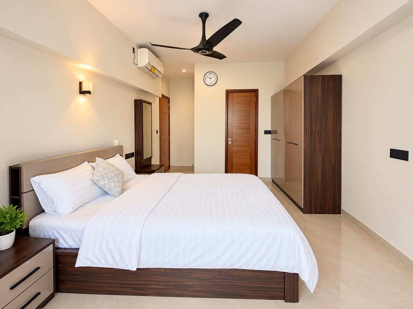 A modern bedroom with a bed, bedside tables, a clock, a ceiling fan, and a wardrobe.