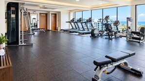 Un gimnasio con cintas de correr, bicicletas estáticas y máquinas de pesas, amplias ventanas con vistas a la ciudad y un diseño interior moderno.
