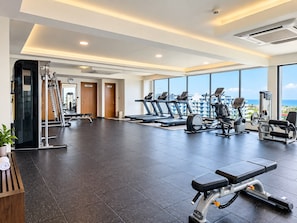 Un gimnasio con cintas de correr, bicicletas estáticas y máquinas de pesas, amplias ventanas con vistas a la ciudad y un diseño interior moderno.