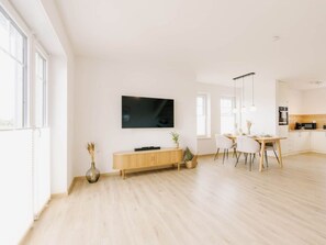 Ein modernes Wohnzimmer mit einem Flachbildfernseher, einer Holzkonsole und einem Essbereich mit Tisch und Stühlen.