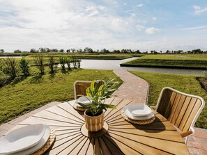 Ein Tisch im Freien mit Stühlen, einem Blumentopf und Blick auf ein Gewässer und Grünflächen.