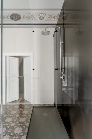 A modern bathroom with a glass shower enclosure, a white door, and patterned floor tiles. - Historic Baroque Palazzo w/Rooftop Terrace, City (Modica)