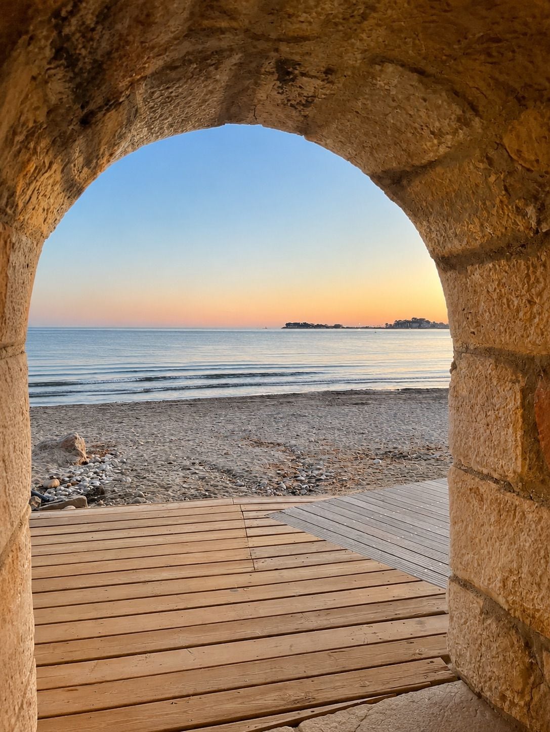 A wooden deck leading to a beach with a stone archway.