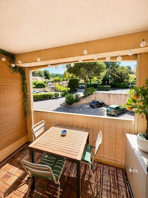Ein Balkon mit Tisch und Stühlen, Blick auf einen Parkplatz und ein Blumentopf.