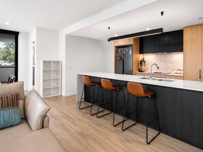 Cozinha moderna com área de bar, sala de jantar com sofá e vista para o exterior.