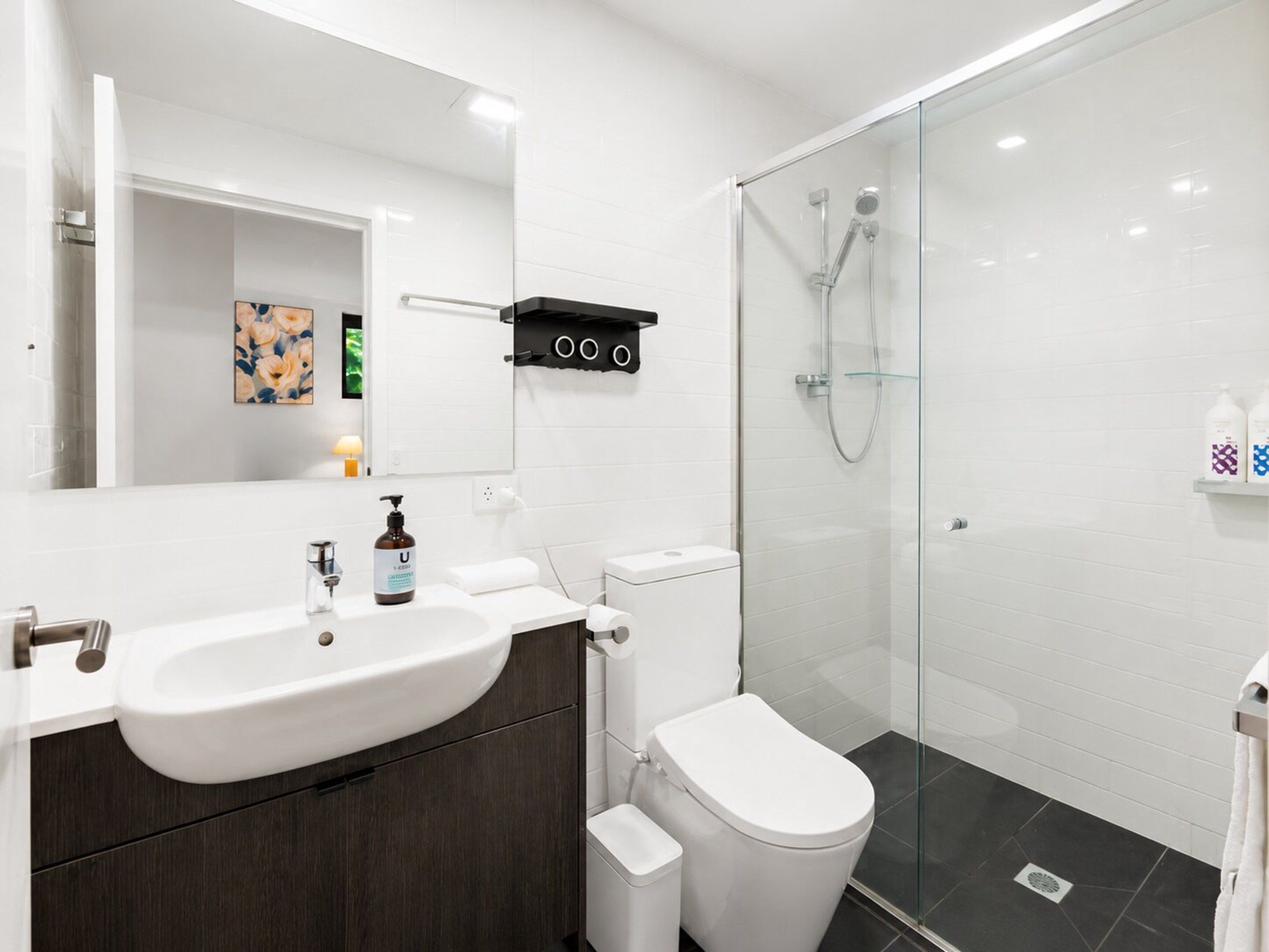 A modern bathroom with a white sink, toilet, and glass-enclosed shower.