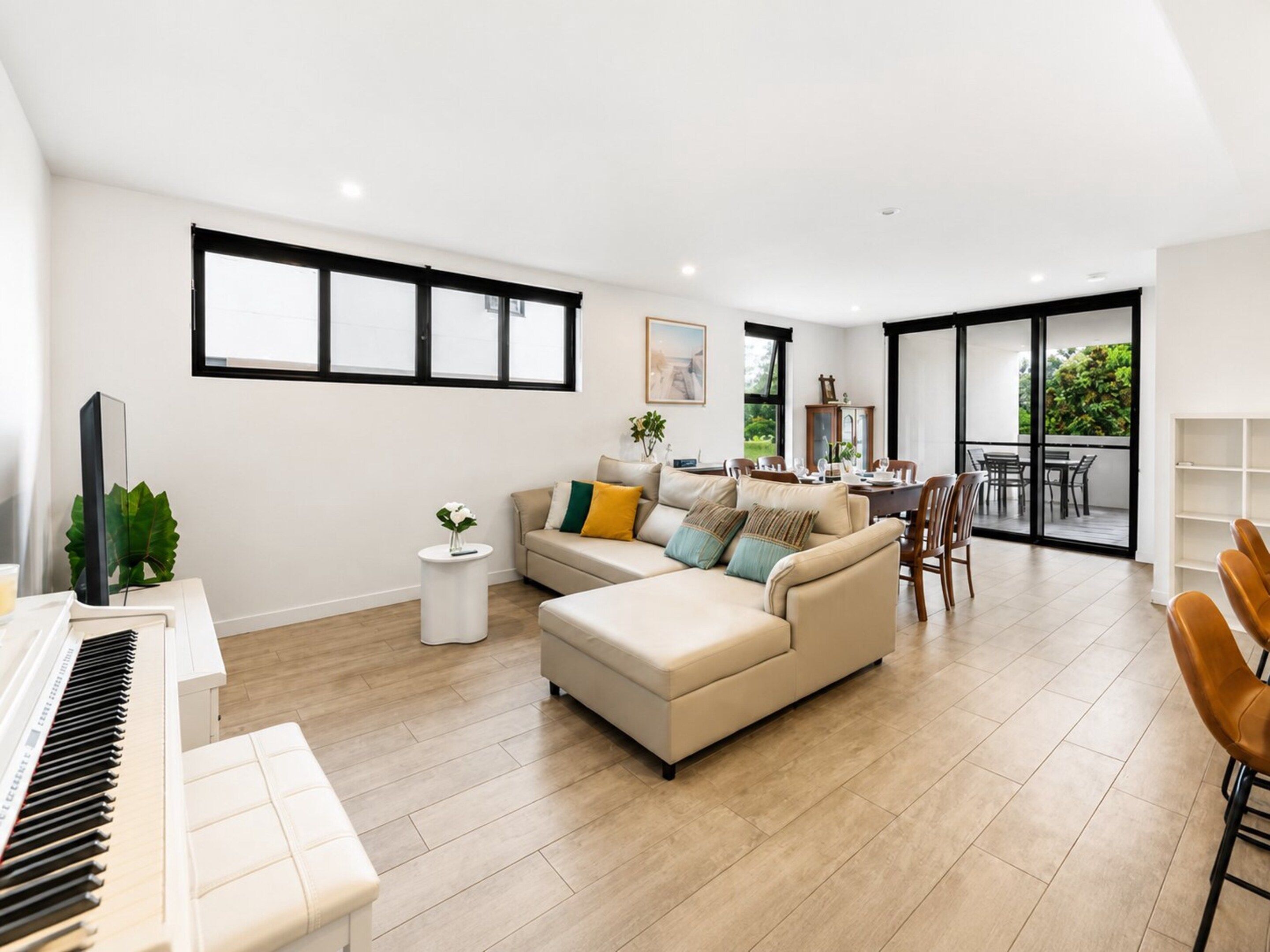 A modern living room with a piano, a sofa set, a dining area, and a balcony with a view.