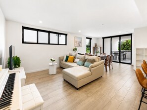 A modern living room with a piano, a sofa set, a dining area, and a balcony with a view. - Elevated 3-bed Apartment Close to Brisbane River (Brisbane)