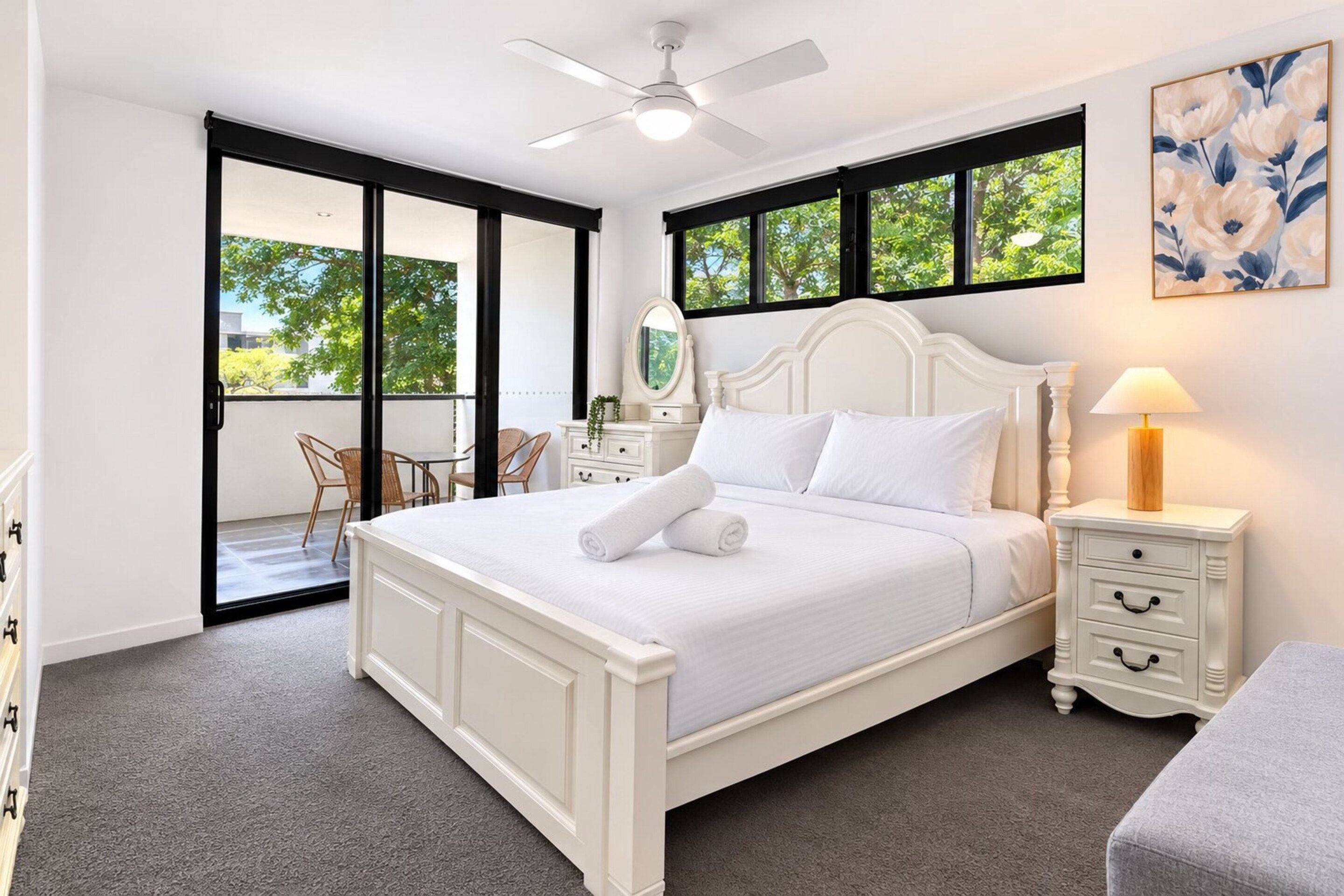 A bedroom with a bed, a nightstand, a lamp, a chair, a mirror, and a sliding glass door leading to an outdoor area.