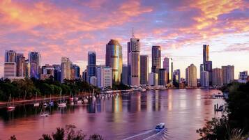 A city skyline with high-rise buildings, a marina with boats, and a river reflecting the sunset.