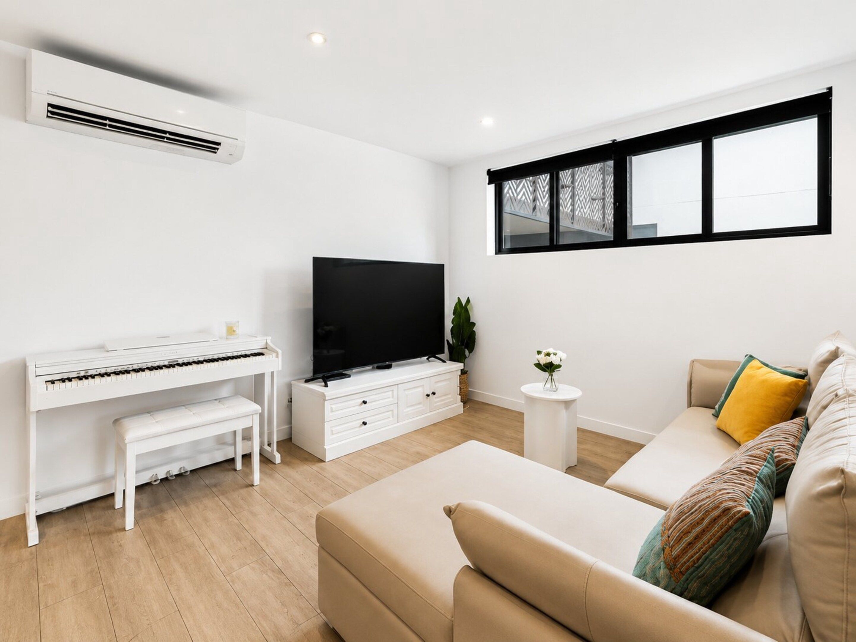 A modern living room with a piano, a flat-screen TV, a sofa, and a window with a view.