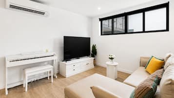 A modern living room with a piano, a flat-screen TV, a sofa, and a window with a view.