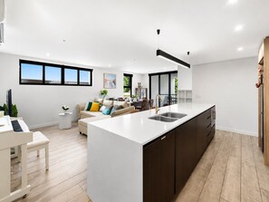 A modern kitchen with a central island, a dining area with a sofa, and a piano. - Elevated 3-bed Apartment Close to Brisbane River (Brisbane)