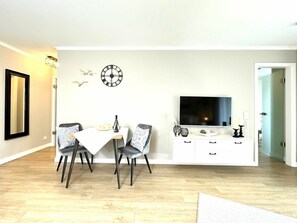 A modern living room with a dining area, a flat-screen TV, and a decorative wall clock. - Logierhaus Friedrich WE 6 (Zingst)