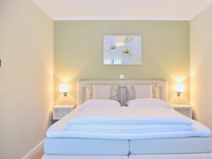 A double bed with a headboard, two bedside lamps, and a wall-mounted artwork. - Logierhaus Friedrich WE 6 (Zingst)