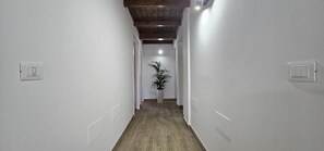A narrow hallway with white walls, wooden flooring, and a potted plant in the center.