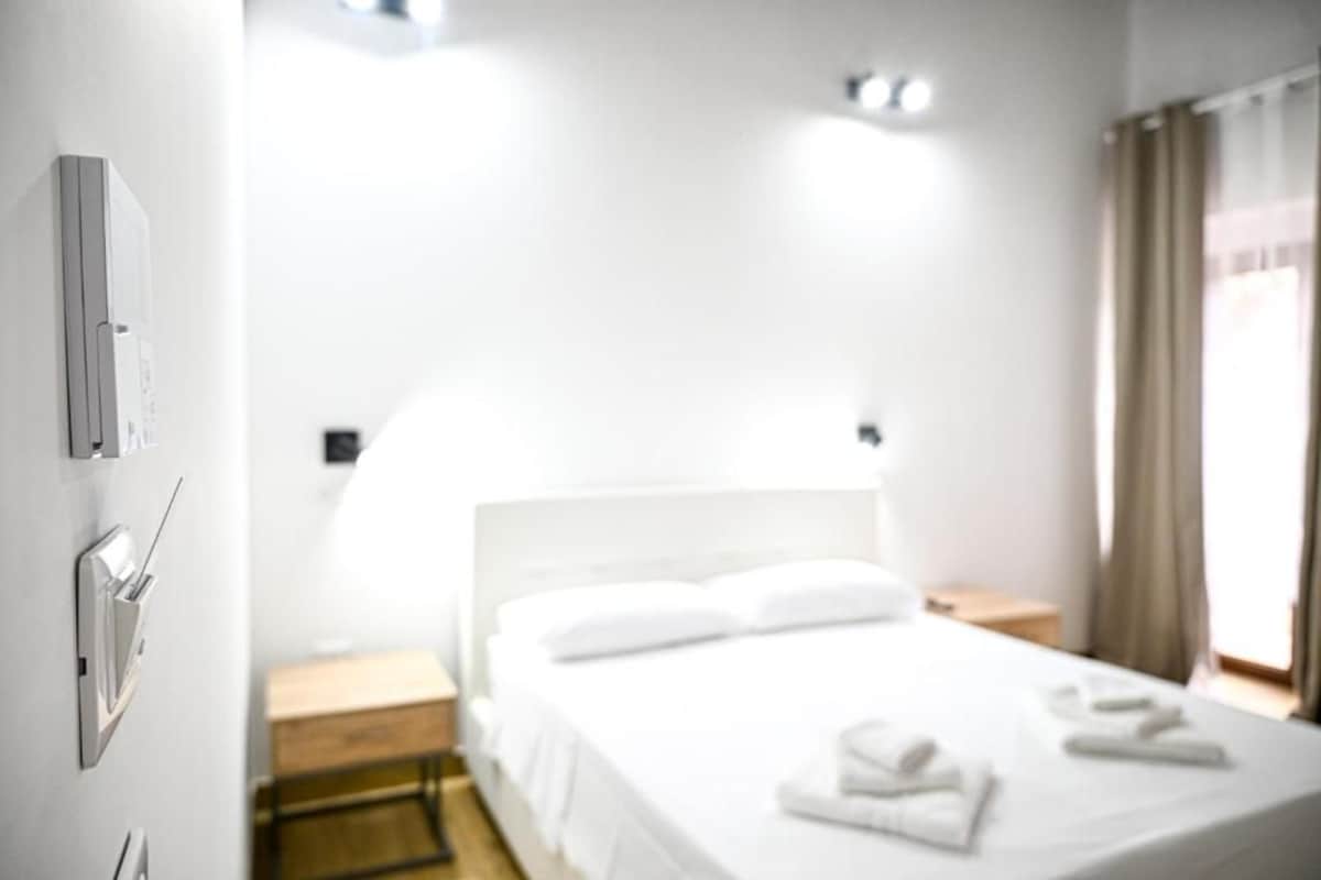 Habitación de hotel con cama, mesita de noche y termostato en la pared.