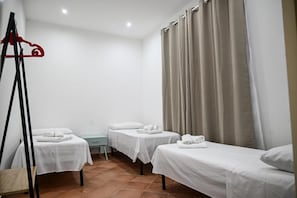 Habitación de hotel con tres camas individuales, una mesita pequeña y un perchero rojo.