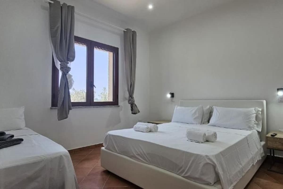 Habitación de hotel con una cama individual, una mesita de noche, una ventana con cortinas y una lámpara de pared.