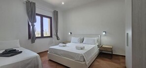Une chambre d’hôtel avec un lit, une table de chevet, une commode et une fenêtre avec des rideaux.