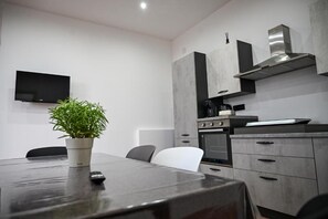 A modern kitchen with a built-in oven, a stainless steel range hood, and a flat-screen TV mounted on the wall.
