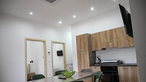 A modern kitchen with wooden cabinets, a built-in oven, and a dining area with a table and chairs. - Borgo Caridà - Green Family Holidays (Zaccanopoli)
