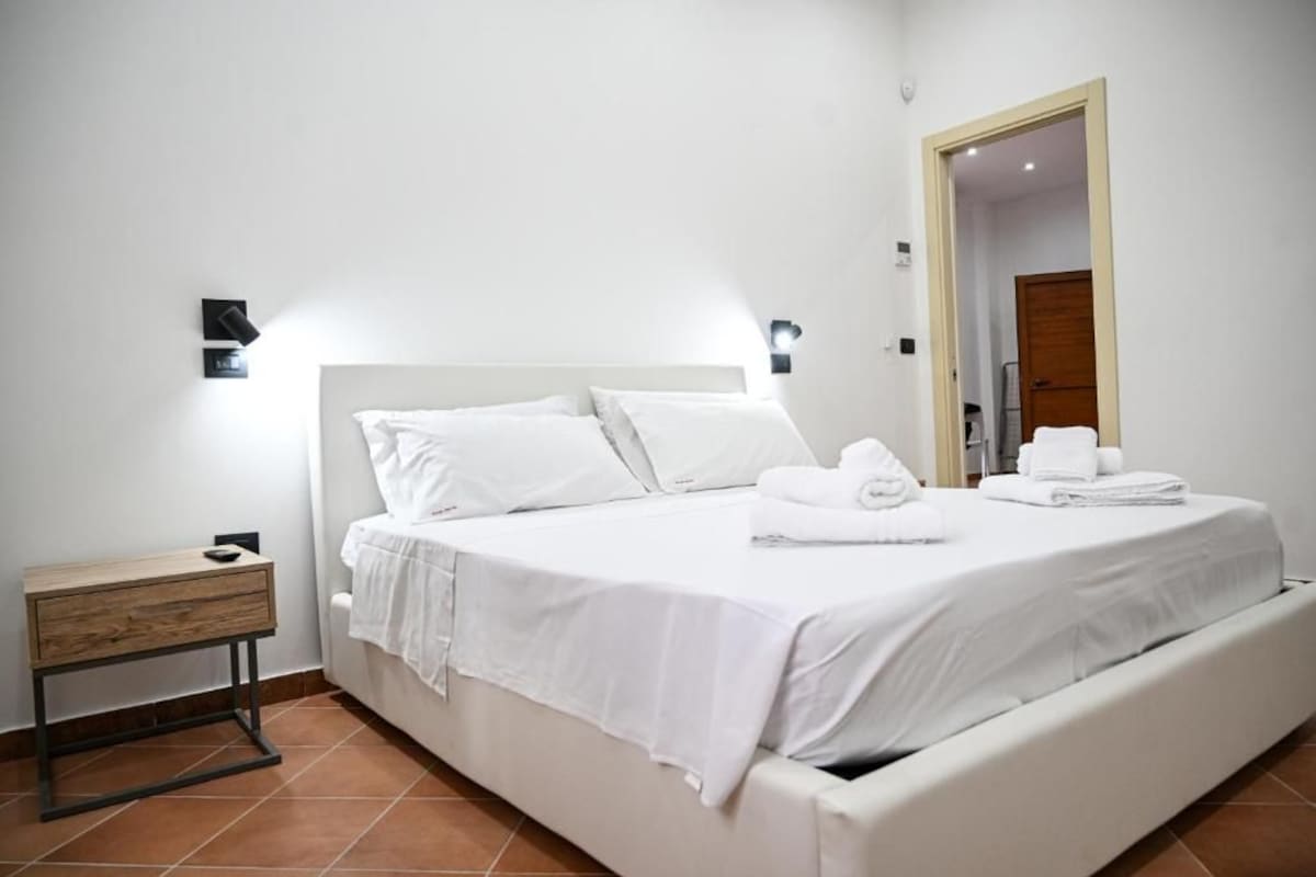 Una habitación de hotel con una cama, una mesita de noche, un espejo y una puerta.