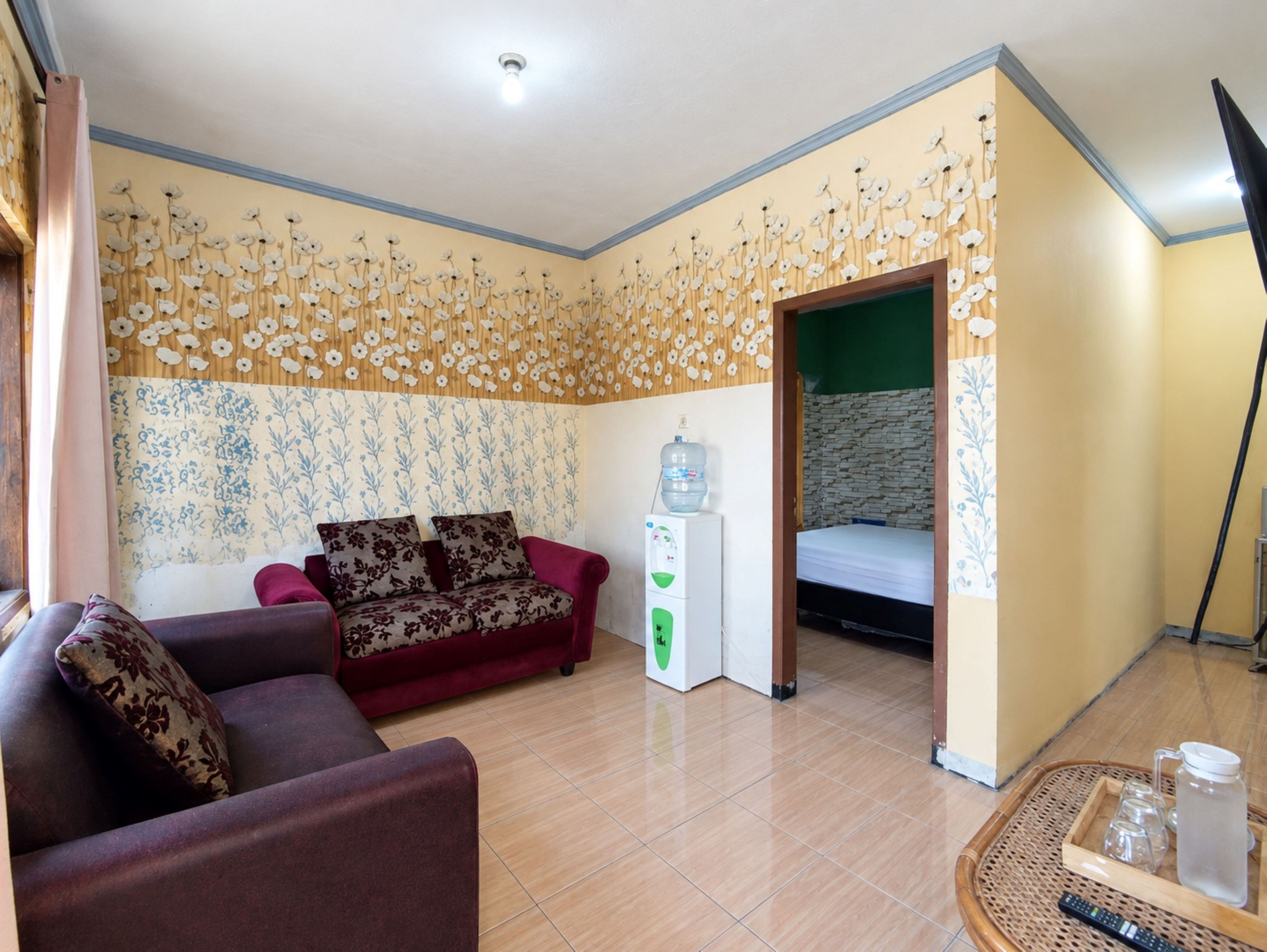 A room with a sofa, a water dispenser, a bed, and a wall with a floral pattern.