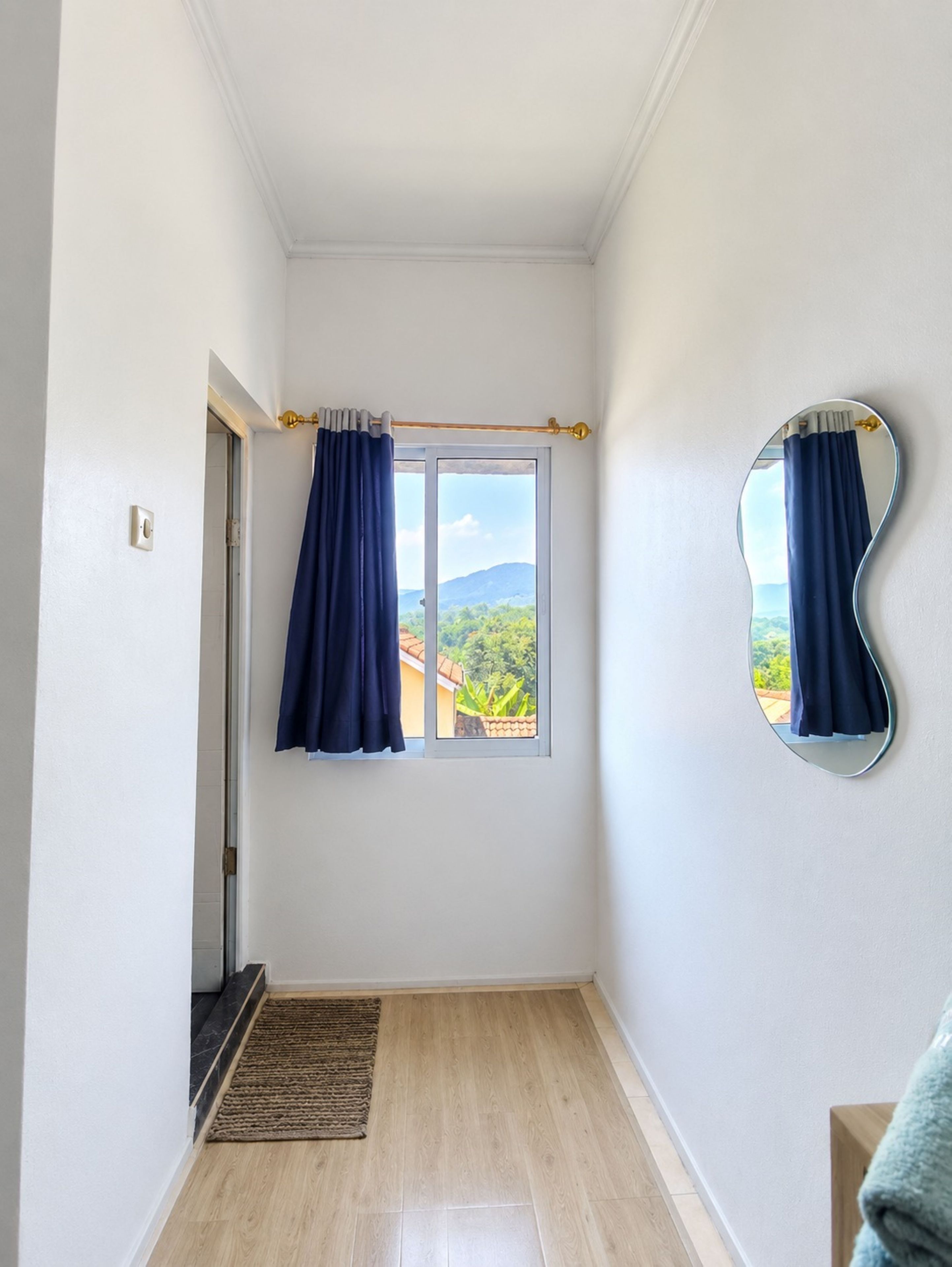 Una habitación con un ventanal grande, un espejo en la pared y una puerta que da a otra estancia.