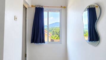 Una habitación con un ventanal grande, un espejo en la pared y una puerta que da a otra estancia.