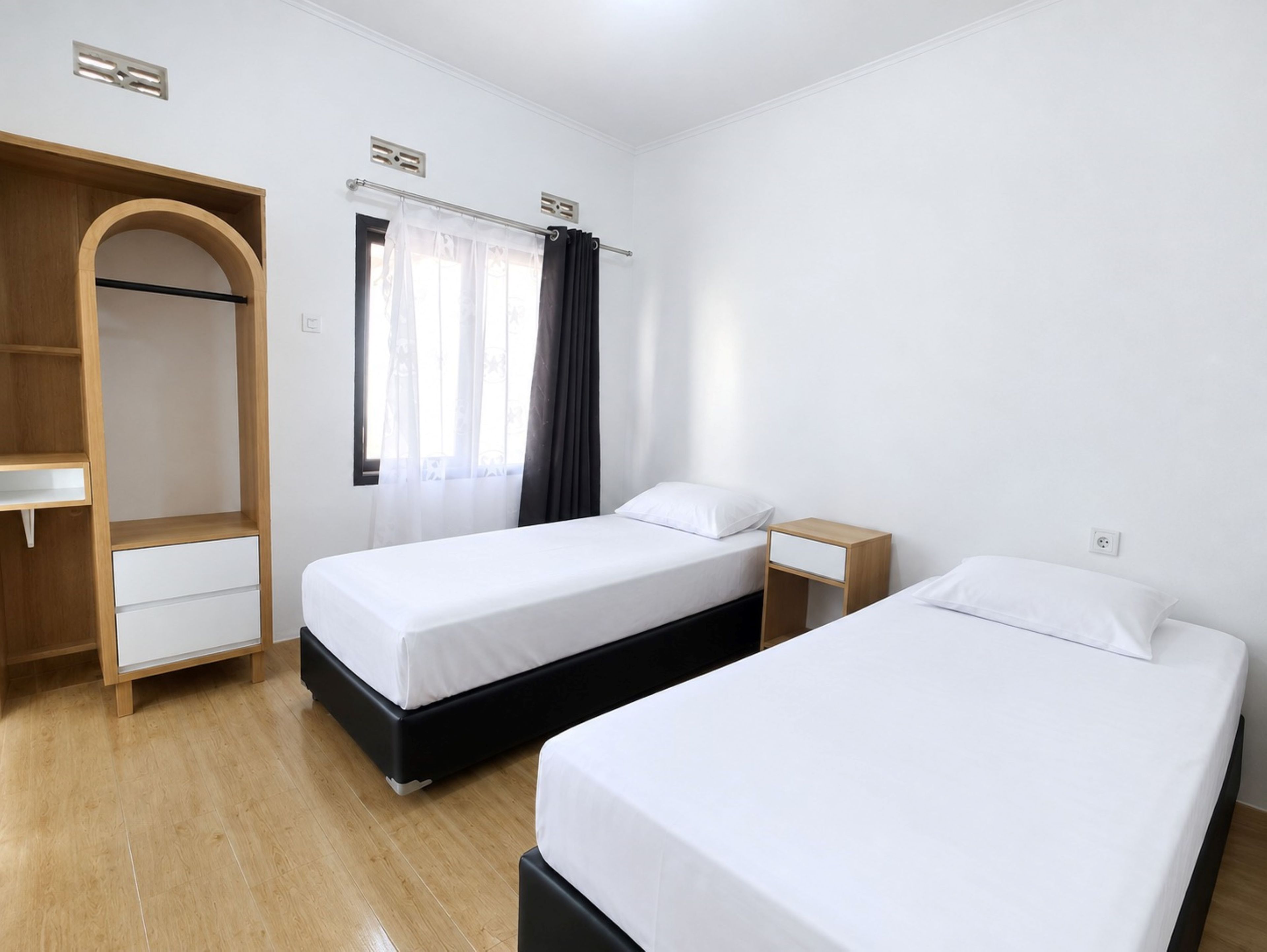 Habitación de hotel con dos camas, un armario de madera, una mesita y una ventana con cortinas.