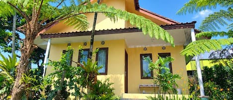 A two-story house with a tiled roof, surrounded by lush greenery and a clear blue sky.