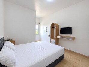 Un dormitorio moderno con cama, mesita de noche, televisor montado en la pared y ventana.