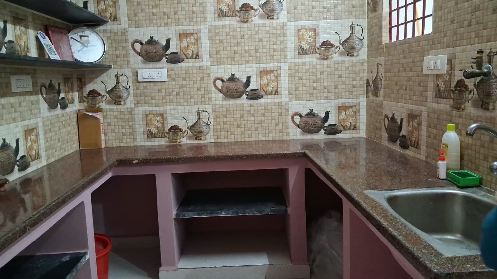 A kitchen with a tiled backsplash featuring teapots, a sink, and a countertop.