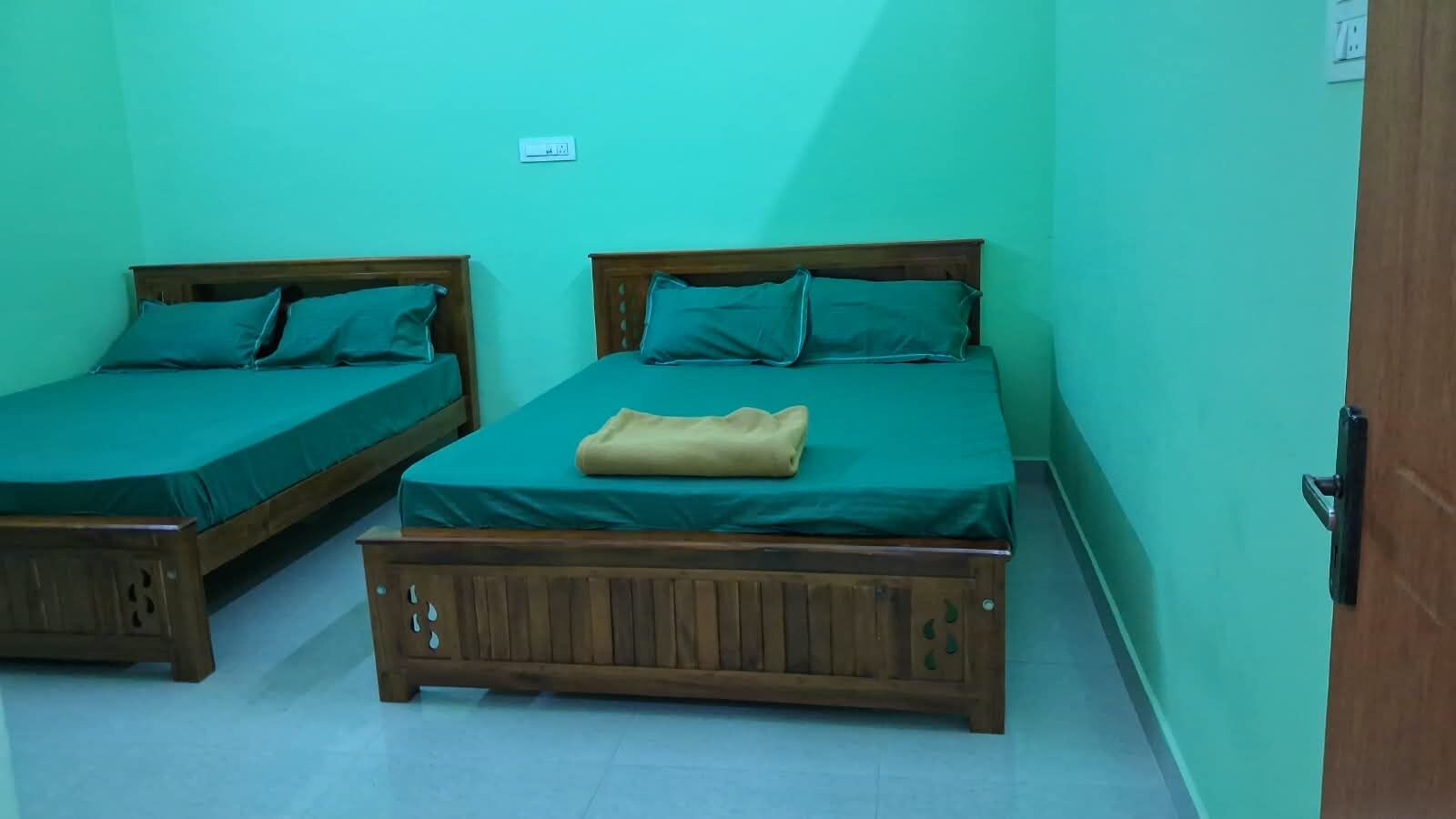 Deux lits en bois, avec une literie verte et une couverture beige, adossés à des murs de couleur turquoise.