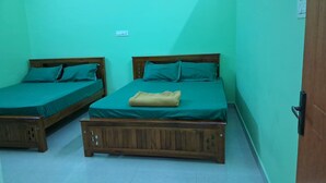 Dos camas de madera con ropa de cama verde y una manta color beige, frente a paredes color turquesa.