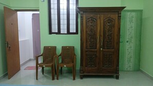 Una habitación con un armario de madera, dos sillas de plástico, un ventanal y una puerta verde.