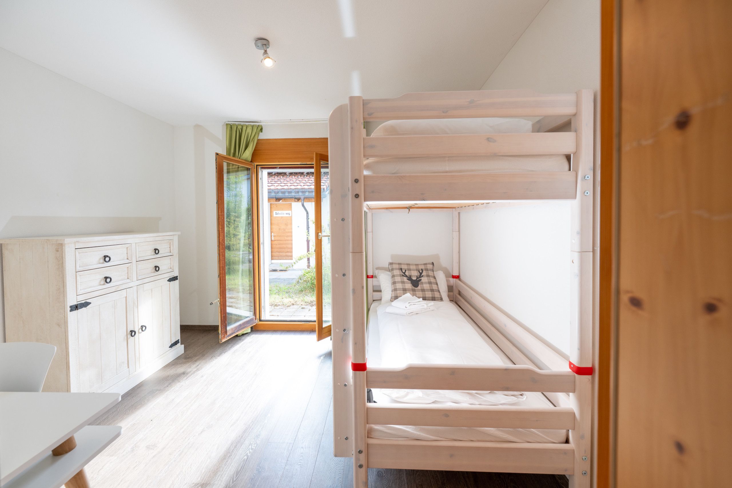 A bunk bed room with a wooden wardrobe and a door leading to an outdoor area.