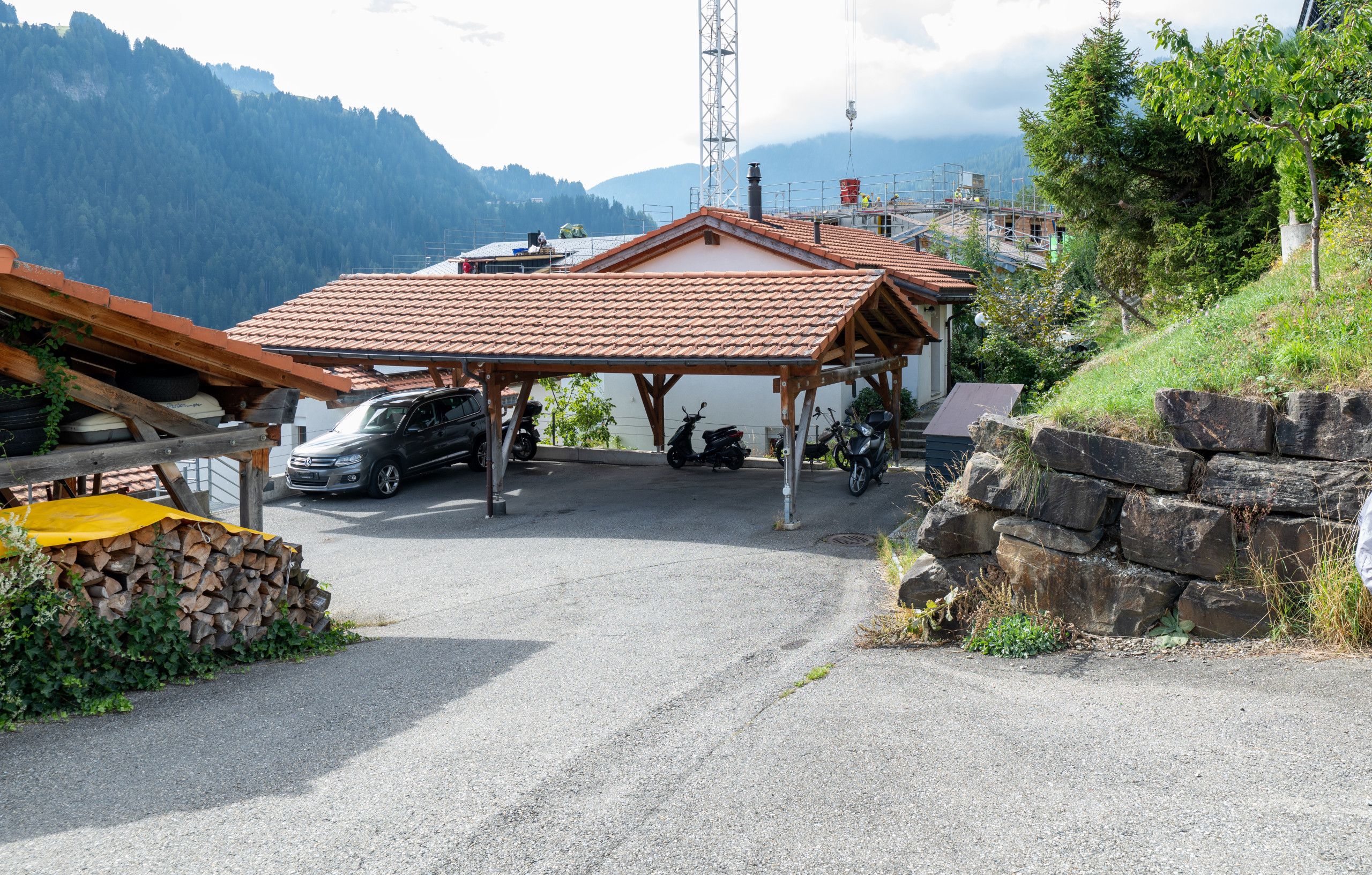A parking area with a covered carport, a motorcycle, and a building with a tiled roof.