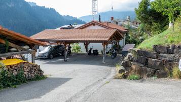 Uma área de estacionamento com abrigo coberto, uma motocicleta e um edifício com telhado em telhas.