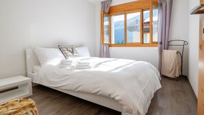 Un lit bien fait, avec du linge de lit blanc, une tête de lit en bois et une fenêtre donnant sur un paysage montagneux.