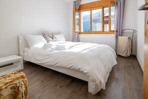 A neatly made bed with white linens, a wooden headboard, and a window with a view of a mountain landscape. - Malix: Apartment with Fireplace & Mountain View (Malix)