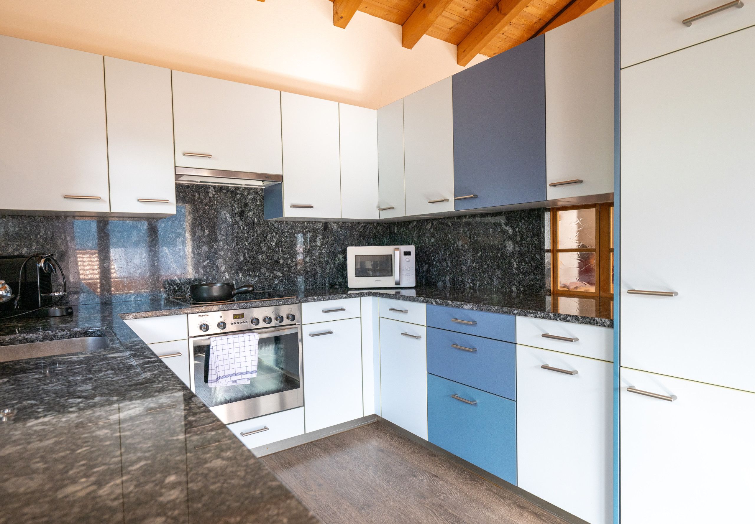 A modern kitchen with white and blue cabinets, a microwave, and a stove.