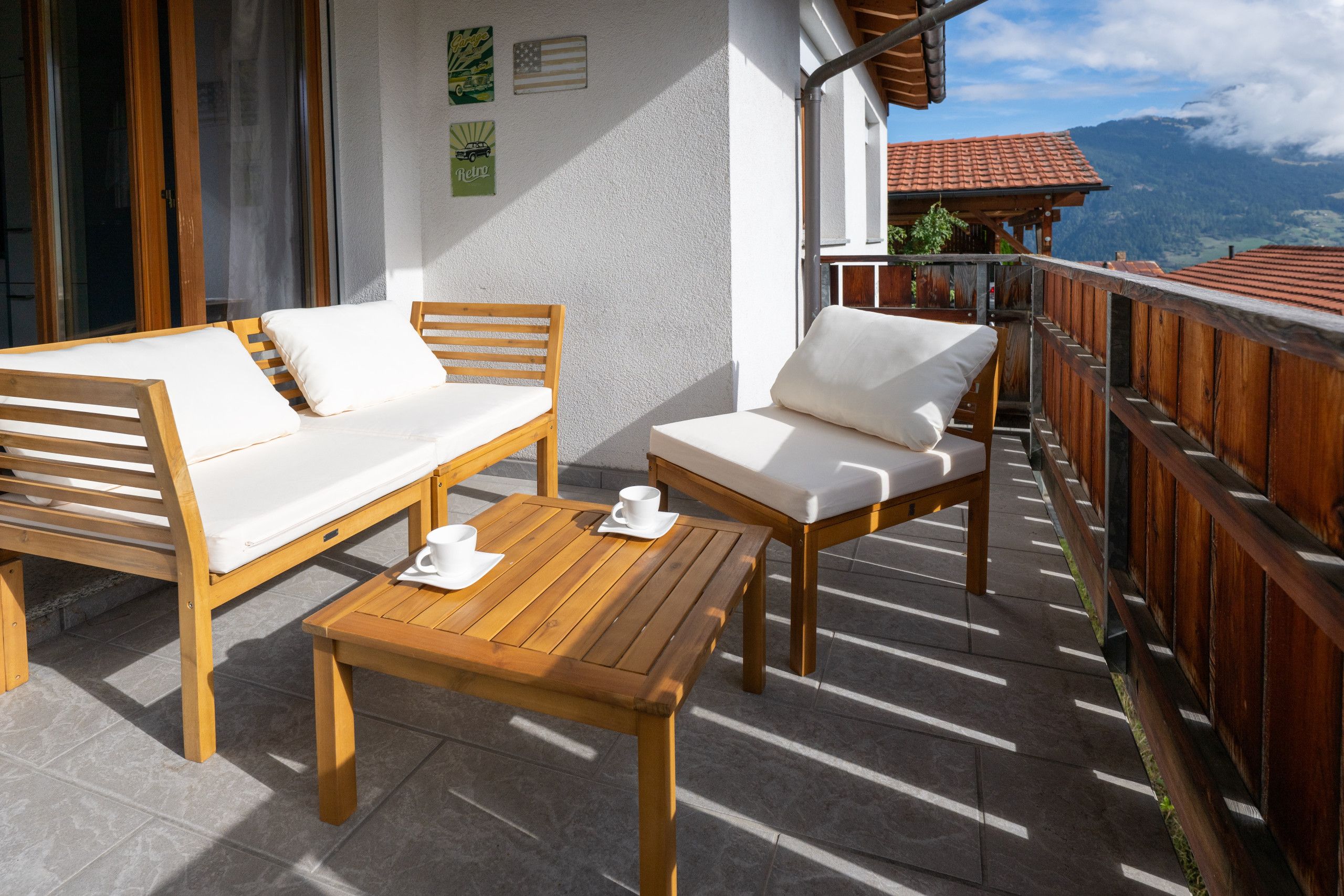 A balcony with wooden furniture, including a sofa and a chair, and a small table with cups.