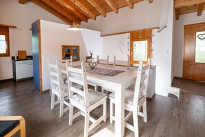 A dining area with a wooden table and chairs, a pendant light, and a window with a view. - Malix: Apartment with Fireplace & Mountain View (Malix)