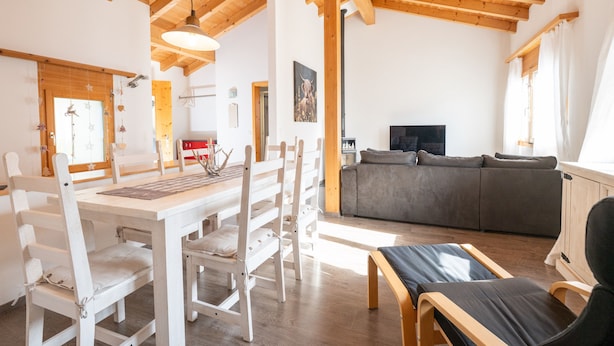 Un vaste espace de vie doté d’un plafond en bois, d’une table à manger avec des chaises, d’un canapé et d’un téléviseur.