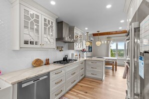 Una cocina moderna con armarios blancos, lavavajillas Bosch, piso de madera y vistas al exterior.