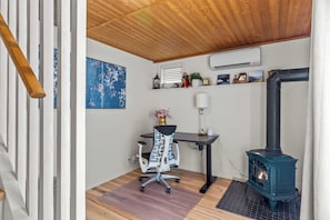 Una stanza con soffitto in legno, una scrivania con una sedia, un condizionatore d'aria a parete, una mensola decorativa con diversi oggetti e una stufa a legna.
